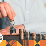 homem branco com um chaveiro em formato de casa na mão e moedas empilhadas na mesa.