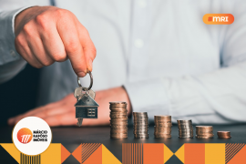 homem branco com um chaveiro em formato de casa na mão e moedas empilhadas na mesa.