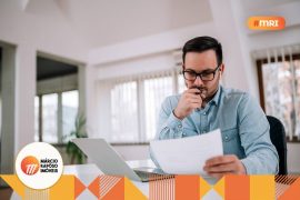 Homem sentado e pensativo, olhando informações em um papel.